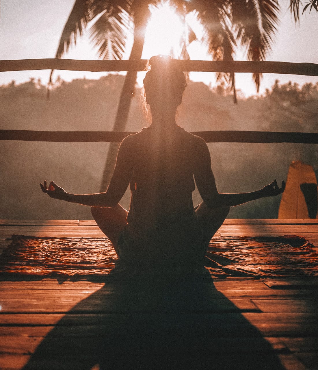 An image of a woman with her back to the camera, in a sitting position, and arms outstreched in a typical meditation pose